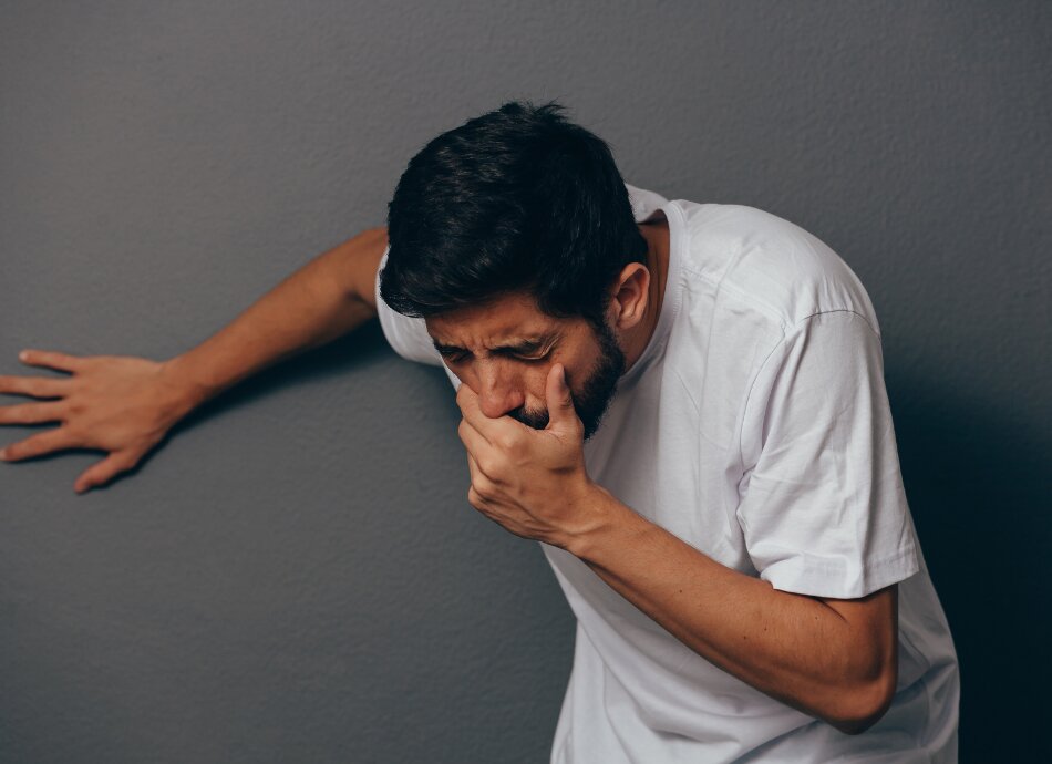 Man leans on wall feeing nauseous with hand over mouth