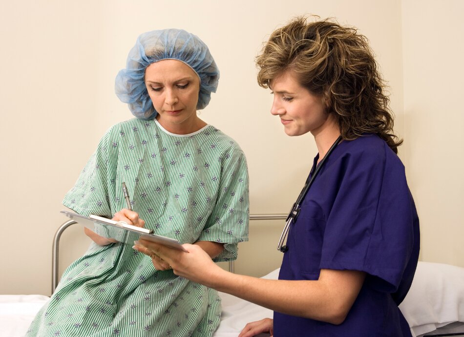 Woman in surgical gown checks pre-surgery consent form with nurse