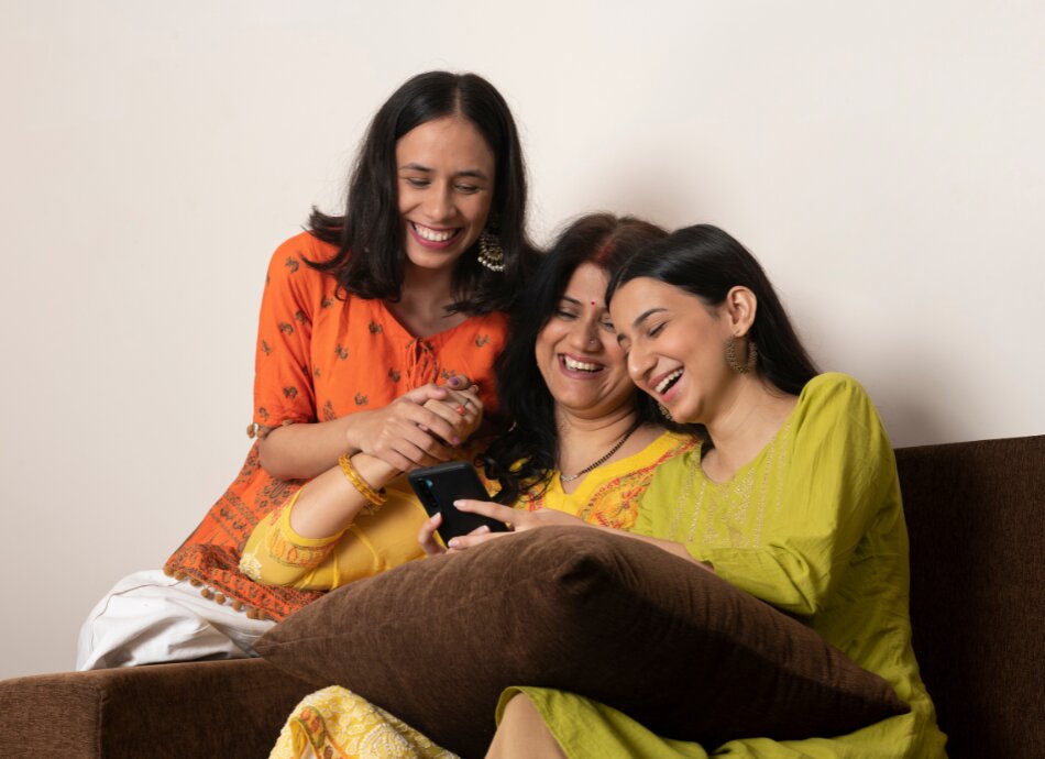 Three Indian women laugh together on couch