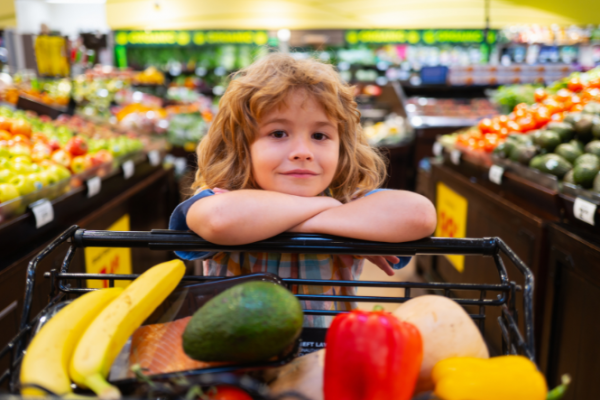 Child rides in the supermarket trolley with fruit 