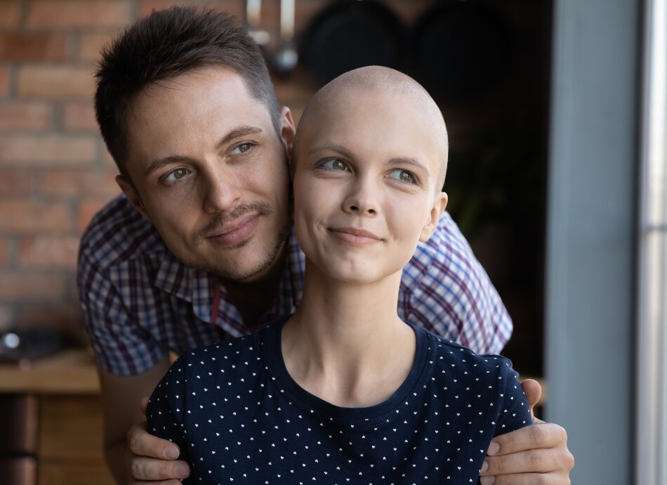 Smiling young man supports hopeful bald woman with cancer