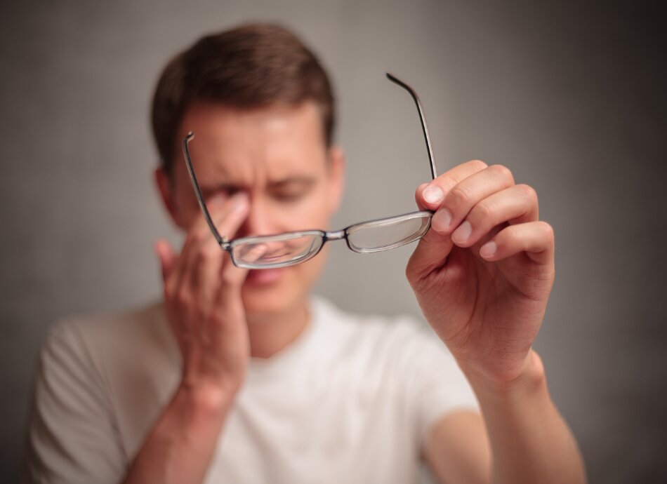 Blurred-out man removes his glasses to rub his eyes