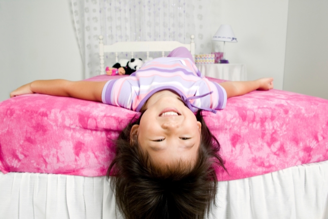 Child lying on bed with head hanging over the edge showing correct position for putting in nose drops