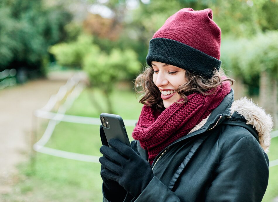 Woman checking phone and smiling outside in winter clothes