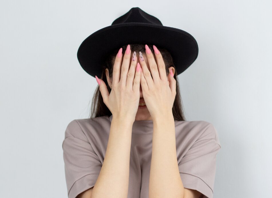 Woman wearing black hat hides face behind her hands