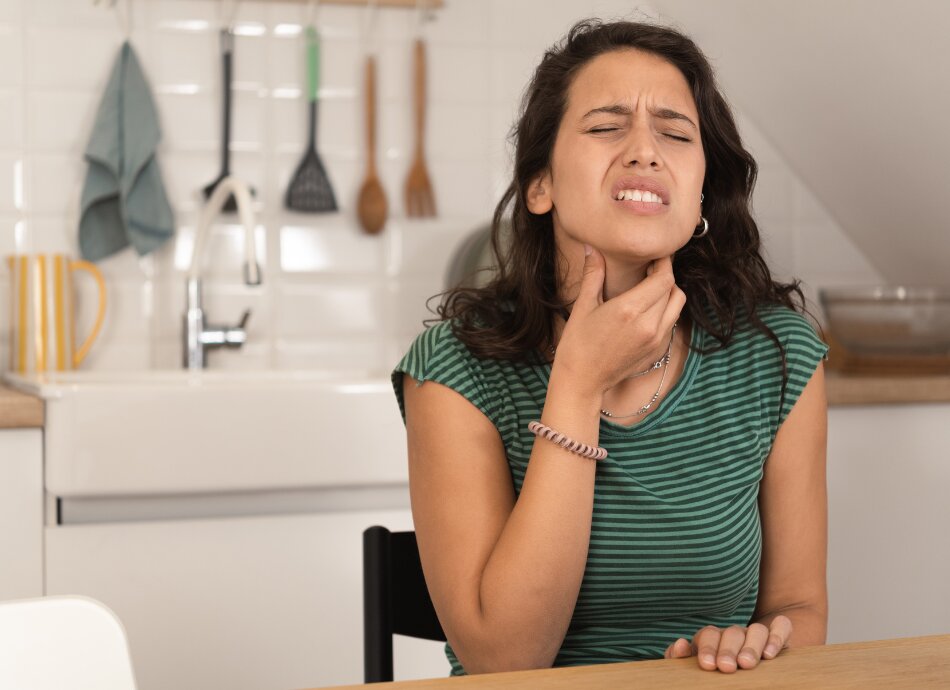 Young woman grimacing and holding sore throat 