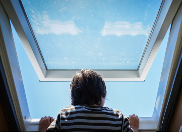 Child looking at the blue sky through an open window
