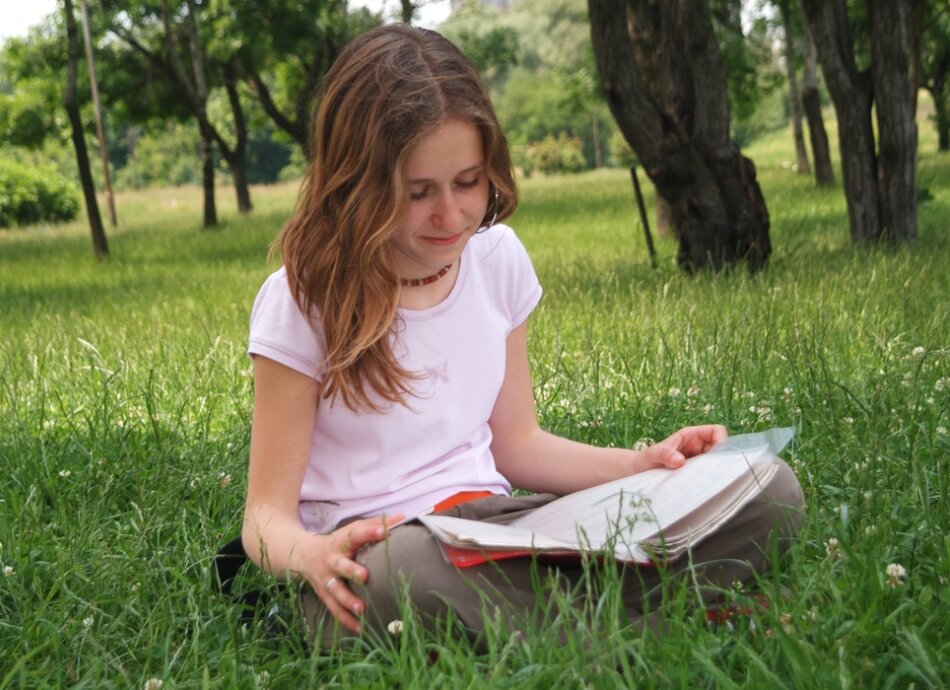 Young girl sitting crosslegged reading book on the grass