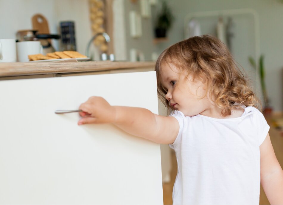 Little girl opens the cupboard to try and find something