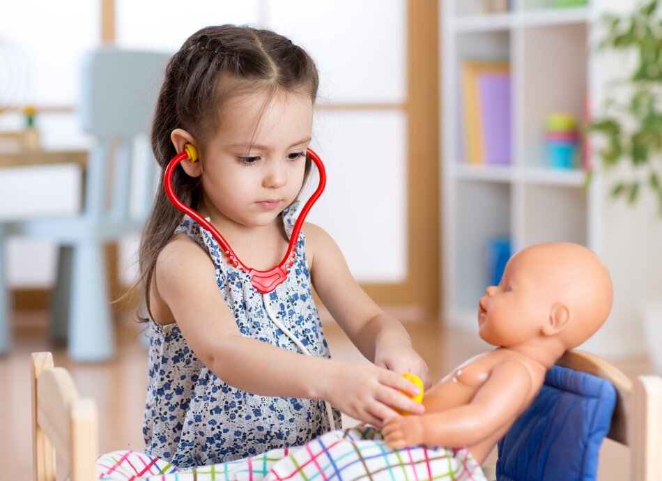 Little girl using toy stethoscope on her doll