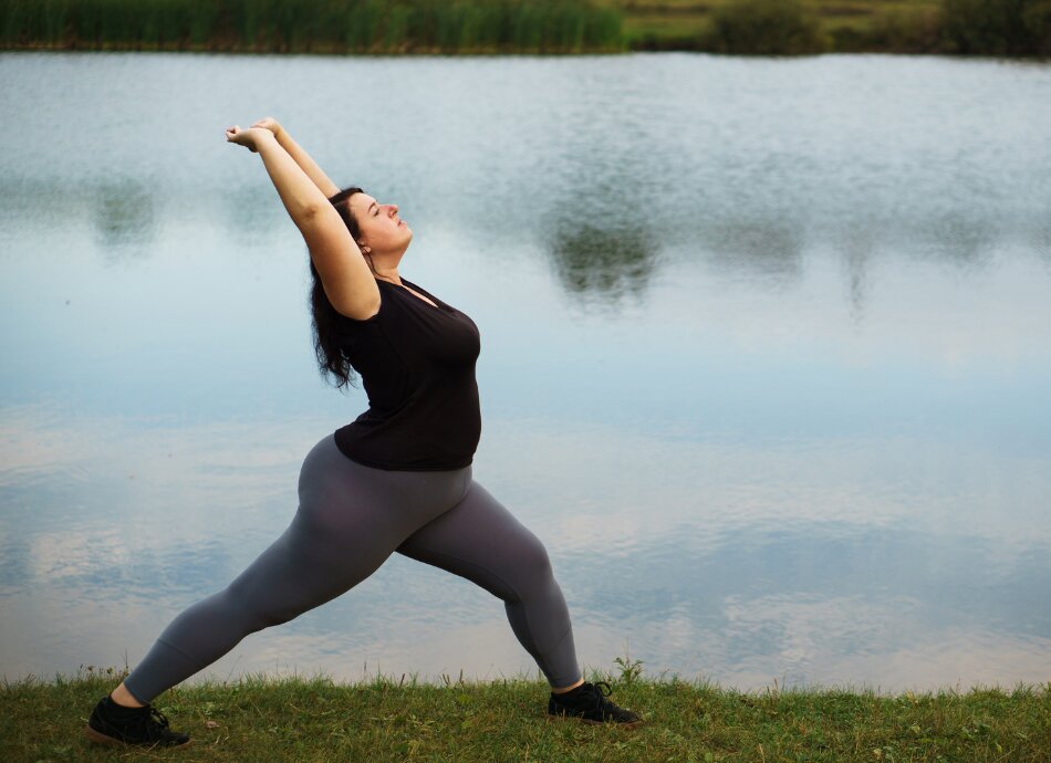Larger woman does yoga pose by the water 