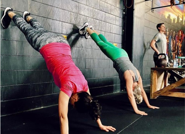 2 women doing handstands exercise against a wall 