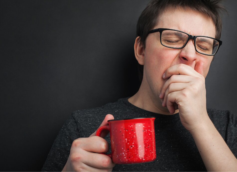 Yawning man holds red coffee cup