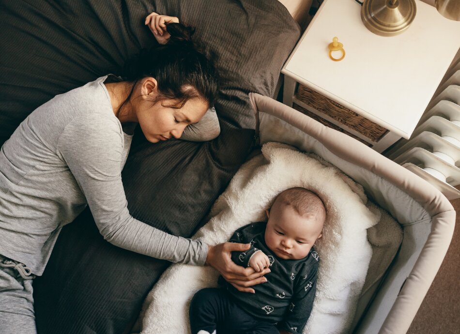 Woman with baby in separate bed beside her 