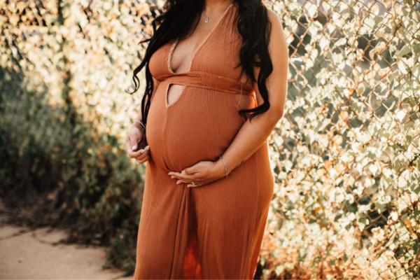 Pregnant woman in brown dress holds her tummy