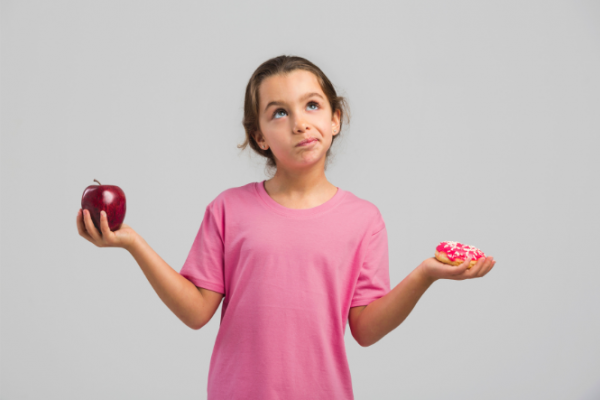 Girl holding apple and doughnut in each hand
