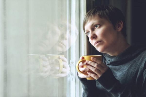 Woman holding mug looks wistfully out window
