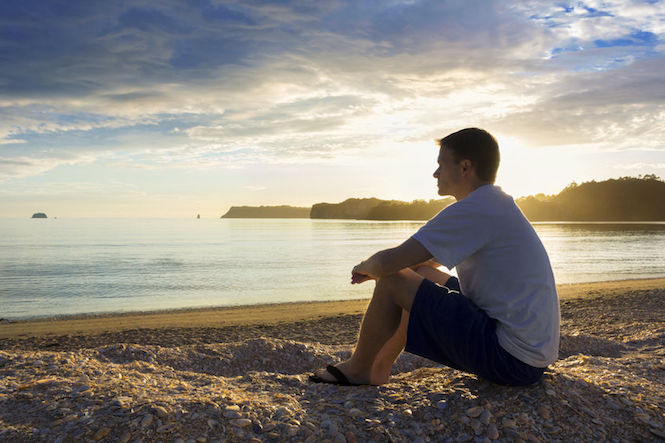 Young man sits on beach at sunrise