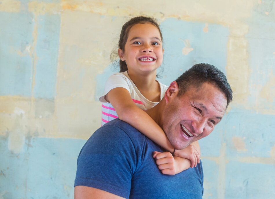 Smiling Pasifika man piggybacking his daughter