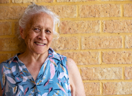 Senior Pasifika woman smiling & leaning against wall